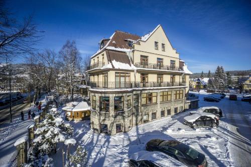 une grande maison avec des voitures garées dans la neige dans l'établissement Willa Excelsior, à Zakopane