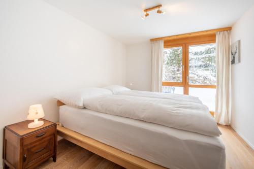 1 dormitorio con 1 cama con mesita de noche y ventana en Casa Collina 5i-02, en Flims