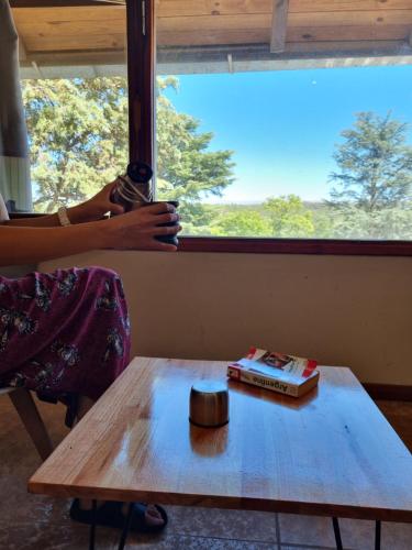 Una mujer mirando por la ventana a una mesa con un libro en Apartamentos Andrea, en Villa General Belgrano