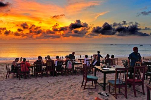 personas sentadas en las mesas de la playa al atardecer en Mango Tree Villas Jimbaran Bali, en Jimbaran