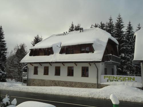 un bâtiment avec un toit enneigé dans la neige dans l'établissement Penzion Dominik, à Železná Ruda