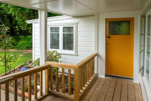 ein Haus mit einer Veranda mit gelber Tür in der Unterkunft Birdsong Cottage in Paraparaumu