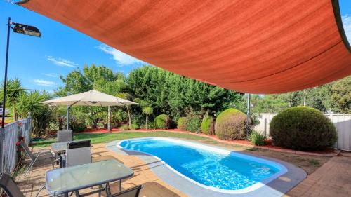 einen Pool mit Sonnenschirm, Tisch und Stühlen in der Unterkunft Glider City Motel Benalla in Benalla