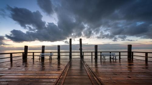 deux bancs sur une jetée avec un ciel nuageux dans l'établissement Lütt Nest Föhr, à Alkersum