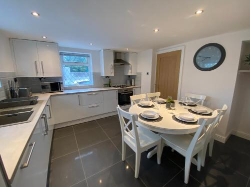 une cuisine avec une table, des chaises et une horloge murale dans l'établissement Modern 4-bed Cottage Llanwrst Town Centre & Parking - Snowdonia! near Betws-y-Coed, à Llanrwst