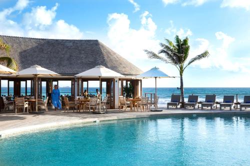 una piscina con tavoli, sedie e l'oceano di Hotel Manapany a Gustavia