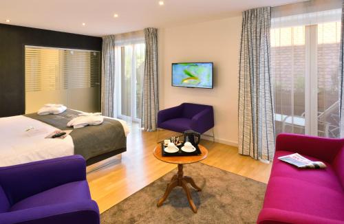 um quarto de hotel com uma cama e duas cadeiras roxas em Logis Hotel Le Parc & Spa em Saint-Hippolyte