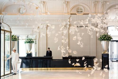 a man in a white suit standing in a lobby with a counter at The Peninsula Paris in Paris