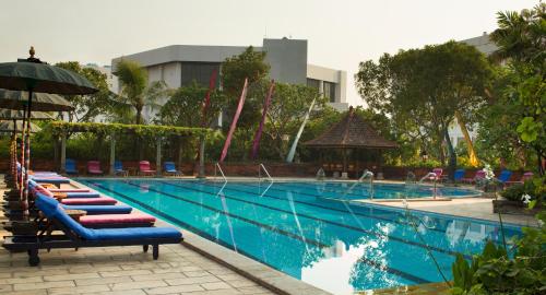 ein großer Pool mit Liegestühlen und einem Sonnenschirm in der Unterkunft Bumi Surabaya City Resort in Surabaya