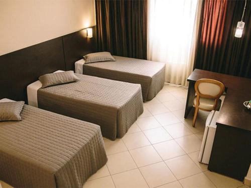 a hotel room with two beds and a chair at Hotel Dunamys Curitiba in Curitiba