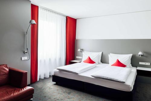 een slaapkamer met een bed met rode kussens en een stoel bij Vienna House Easy by Wyndham Stuttgart in Stuttgart