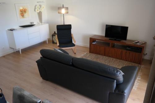 uma sala de estar com um sofá preto e uma televisão em Vila Atlantida Apartment em Vilamoura