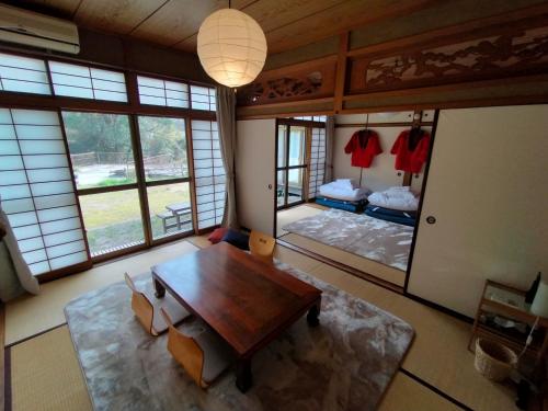 ein Wohnzimmer mit einem Tisch, einem Bett und Fenstern in der Unterkunft 88 House Hiroshima in Hiroshima