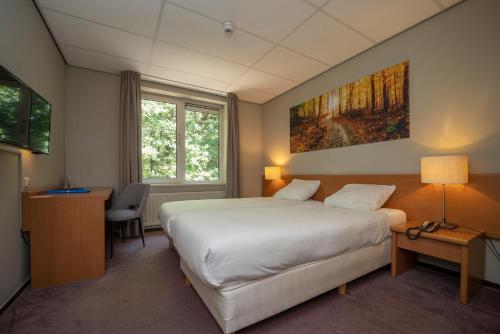 um quarto de hotel com uma cama, uma secretária e uma janela em Fletcher Hotel Restaurant Boschoord em Oisterwijk