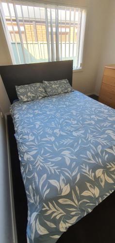 a bed with a blue and white comforter and a window at Home stay in Wyndham Vale