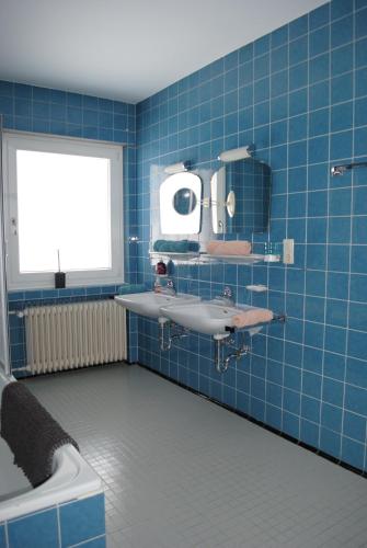 La salle de bains est pourvue de carrelage bleu, d'un lavabo et d'un miroir. dans l'établissement Landhaus Steinbrech, à Grainau