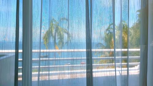 ein Fenster mit Blick auf den Strand und Palmen in der Unterkunft มารินอส บีชเฮ้าส์ Marinos Beach house in Si Racha