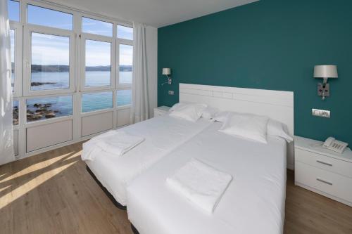 een slaapkamer met een wit bed en een blauwe muur bij Hotel Mar de Fisterra in Finisterre