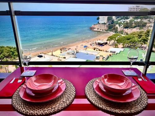 - une table avec 2 assiettes rouges et des verres à vin ainsi qu'une plage dans l'établissement Blue Salou, à Salou