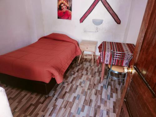 1 dormitorio con cama roja y mesa en Hostal Raymi, en Ollantaytambo