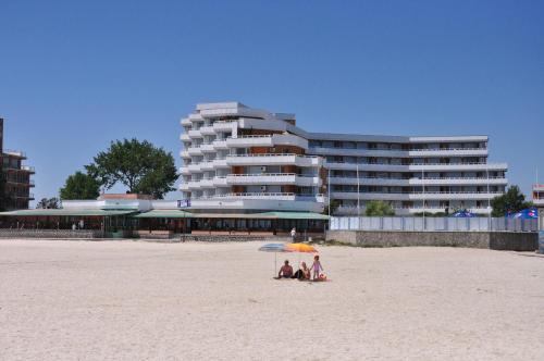 two people sitting under an umbrella on the beach at Hotel Lido in Mamaia