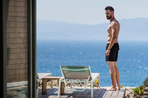 een man op een balkon met uitzicht op de oceaan bij KLIDON Dreamy Living Suites in Mykonos-stad