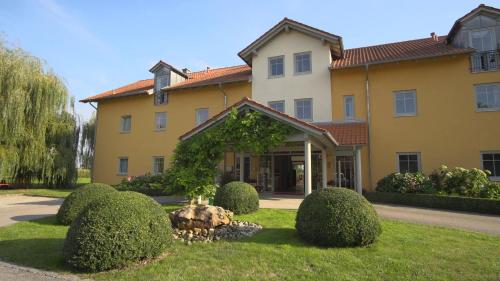 un grand bâtiment jaune avec des buissons devant lui dans l'établissement Landhotel Larenzen, à Kirchham