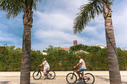 un hombre y una mujer montando en bicicleta entre dos palmeras en Hotel Neptuno, en Atouguia da Baleia