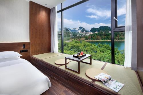 ein Schlafzimmer mit einem großen Fenster mit einem Bett und einem Tisch in der Unterkunft Riverside Wing Hotel Guilin in Guilin