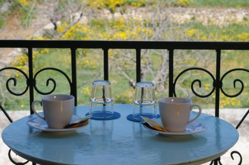 a table with two cups and two glasses on a balcony at Hotel Aegina in Aegina Town