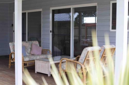 une terrasse couverte avec un canapé et des chaises sur une maison dans l'établissement Magnolia Cottage, à Coffs Harbour