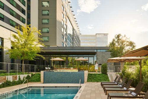 uma piscina com cadeiras e guarda-sóis ao lado de um edifício em Houston CityPlace Marriott at Springwoods Village em The Woodlands