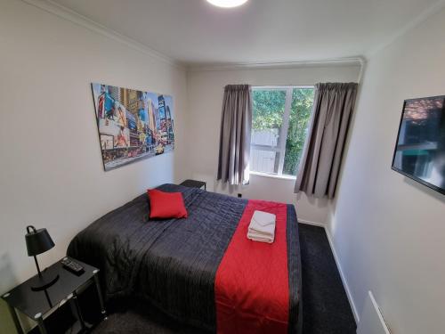 a bedroom with a bed with a red blanket and a window at Stay Timaru in Timaru