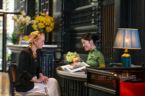 duas mulheres sentadas numa mesa com um livro em Scent Premium Hotel em Hanói