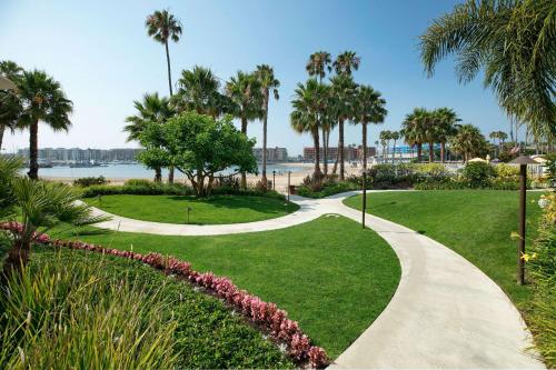 a walkway through a park with palm trees and a beach at Jamaica Bay Inn Marina Del Rey Tapestry Collection by Hilton in Los Angeles