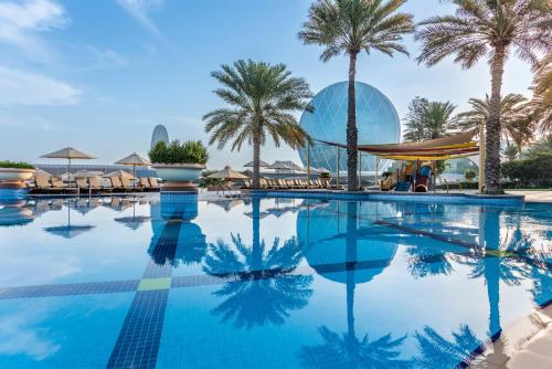 een zwembad met palmbomen en een gebouw bij Al Raha Beach Hotel in Abu Dhabi