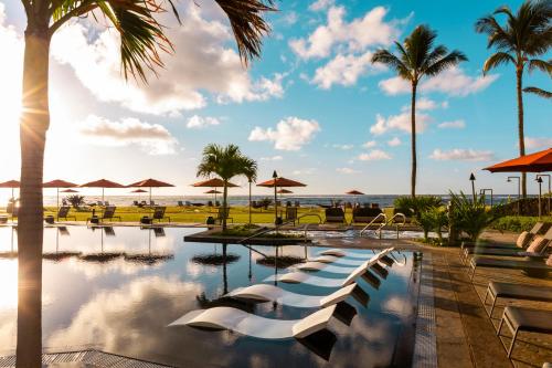 een zwembad in een resort met palmbomen en de oceaan bij Sheraton Kauai Coconut Beach Resort in Kapaa