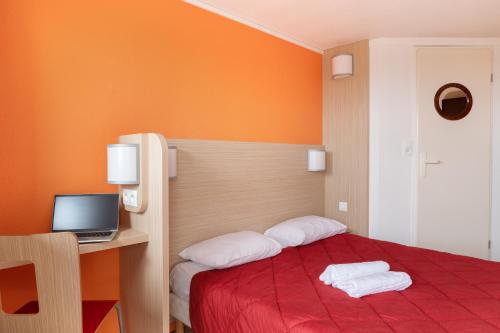 een slaapkamer met een rood bed en een bureau met een laptop bij Premiere Classe La Ville Du Bois in La Ville-du-Bois