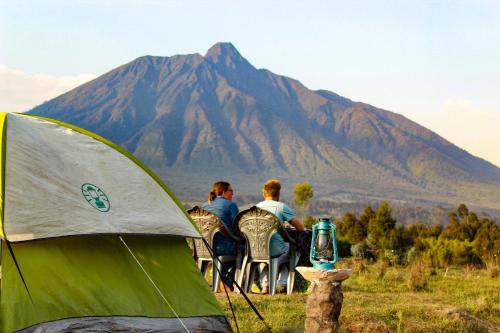 un groupe de personnes assis sur des chaises devant une montagne dans l'établissement Under Volcanoes View Guest House, à Nyarugina