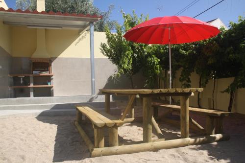 einen Picknicktisch mit einem roten Regenschirm und einer Bank in der Unterkunft CasaTioManel in Amiães de Baixo