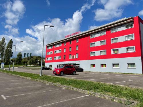 un bâtiment rouge avec une voiture garée dans un parking dans l'établissement Enzo Hotels Thionville by Kyriad Direct, à Thionville