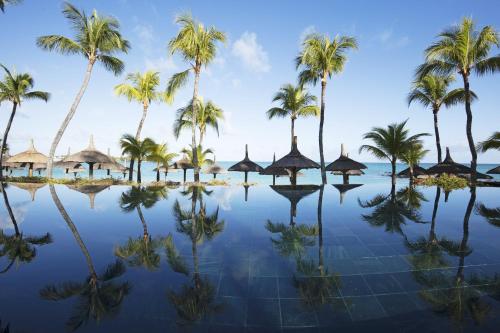 a resort pool with palm trees and huts at Royal Palm Beachcomber Luxury in Grand Baie