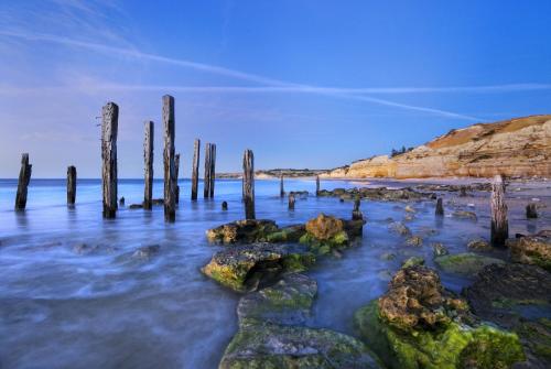 une plage avec des poteaux en bois dans l'eau dans l'établissement BIG4 Port Willunga Tourist Park, à Aldinga