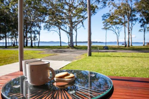 ein Glastisch mit einer Tasse und etwas Brot darauf in der Unterkunft 'Swan Cottage' Port Stephens Waterfront Solace in Newcastle