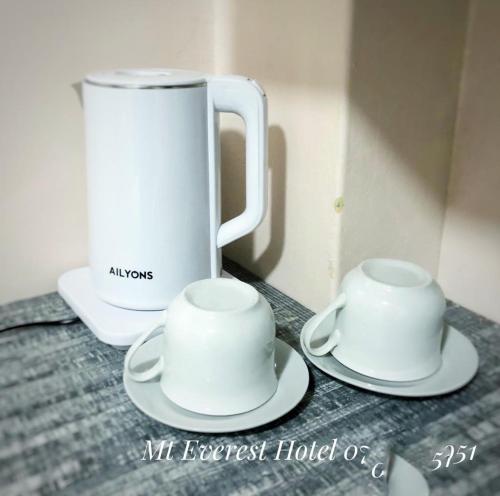 two white cups and saucers on a table with a jug at Mt. Everest Hotel in Kisii