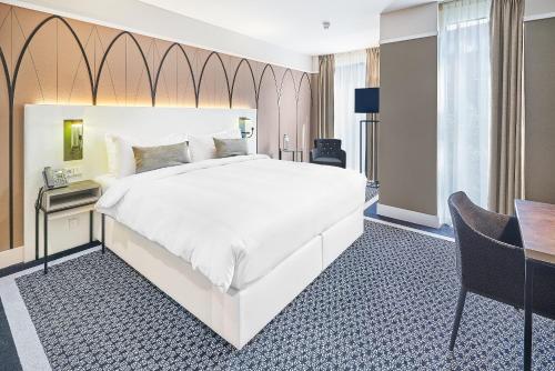 a bedroom with a large white bed and a desk at Hotel Nassau Breda, Autograph Collection in Breda