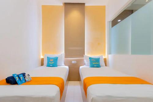 2 camas en una habitación con almohadas de color naranja y azul en Sans Hotel Box Mansion Surabaya by RedDoorz, en Wonokitri 2