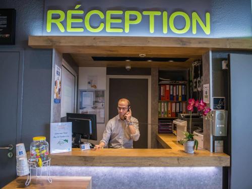 a man sitting at a counter talking on a cell phone at ibis budget Site du Futuroscope in Chasseneuil-du-Poitou