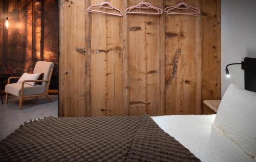 a bedroom with a wooden wall with a bed and a chair at Hôtel-Restaurant Le Cochon Rose in La Sagne