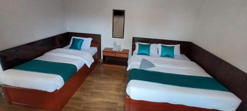 2 łóżka w pokoju z niebieskimi i zielonymi poduszkami w obiekcie Hotel Dolly w mieście Pokhara